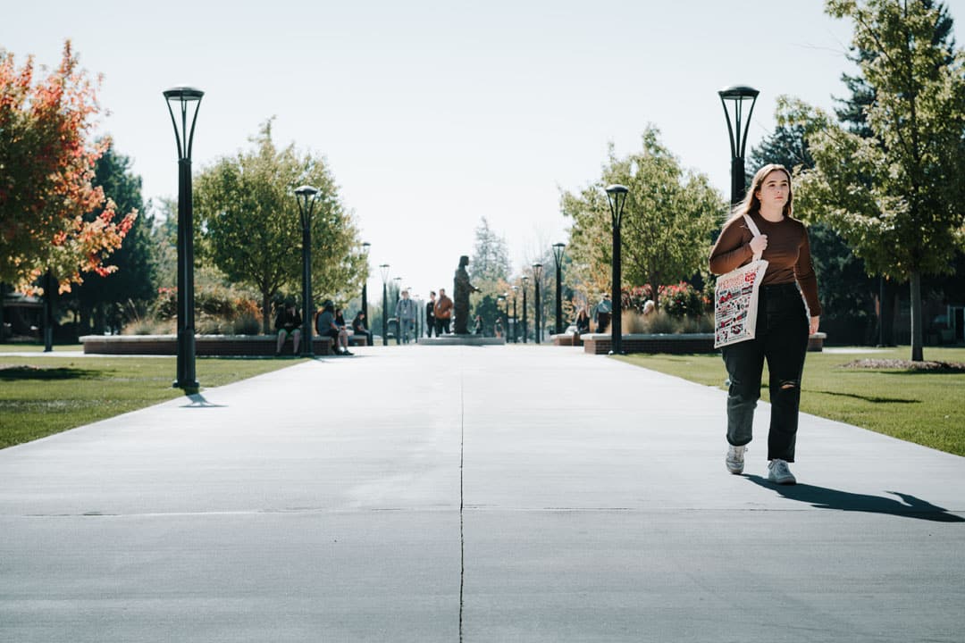 student walking on sidewalk with tote bag