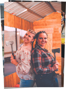 girls standing back to back at axe throwing