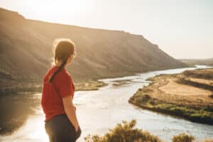 a female student stands on the edge of a bluff looking out at the Snake River at sunset