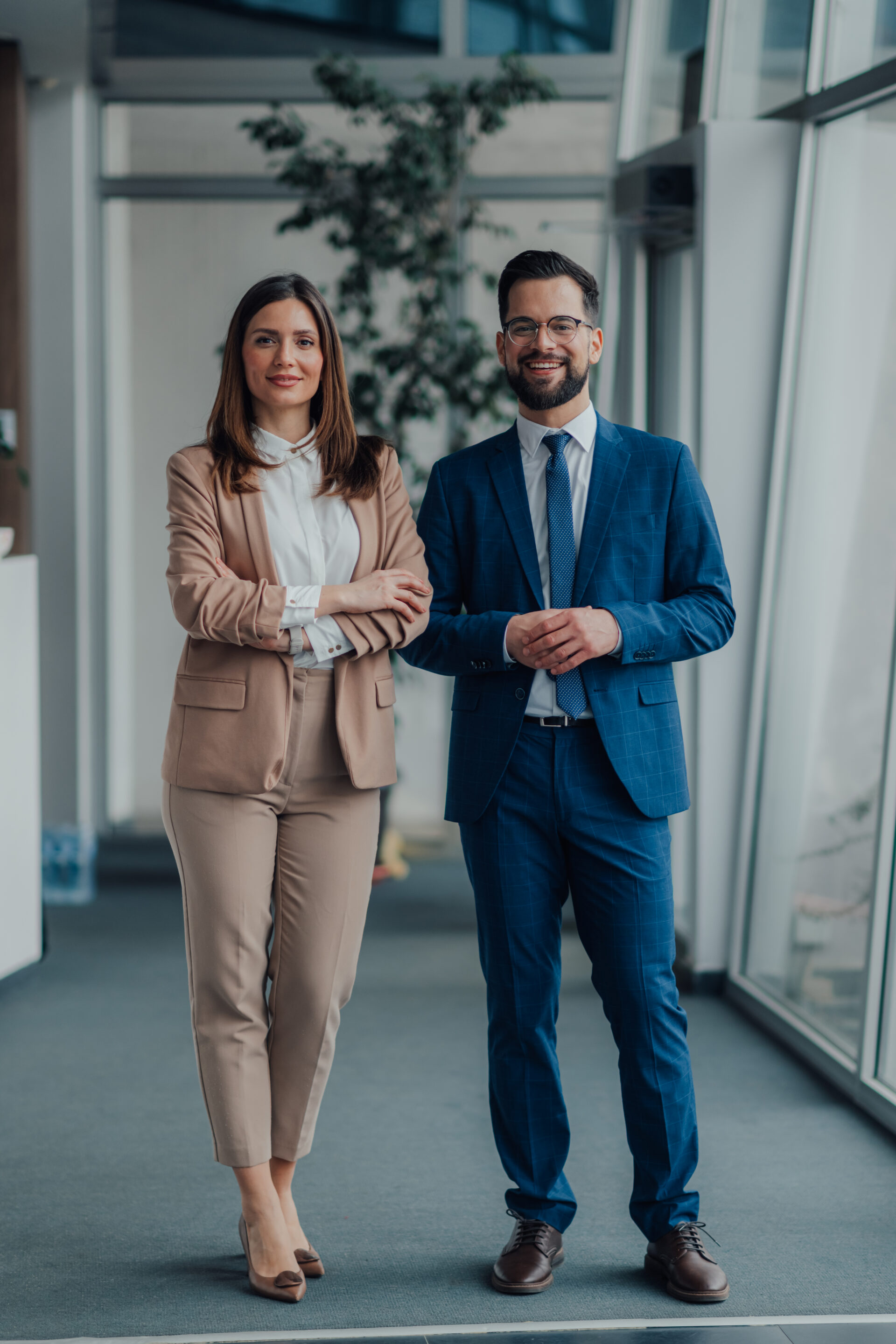 Full-length portrait of two business people smiling and posing confidently in a modern office environment